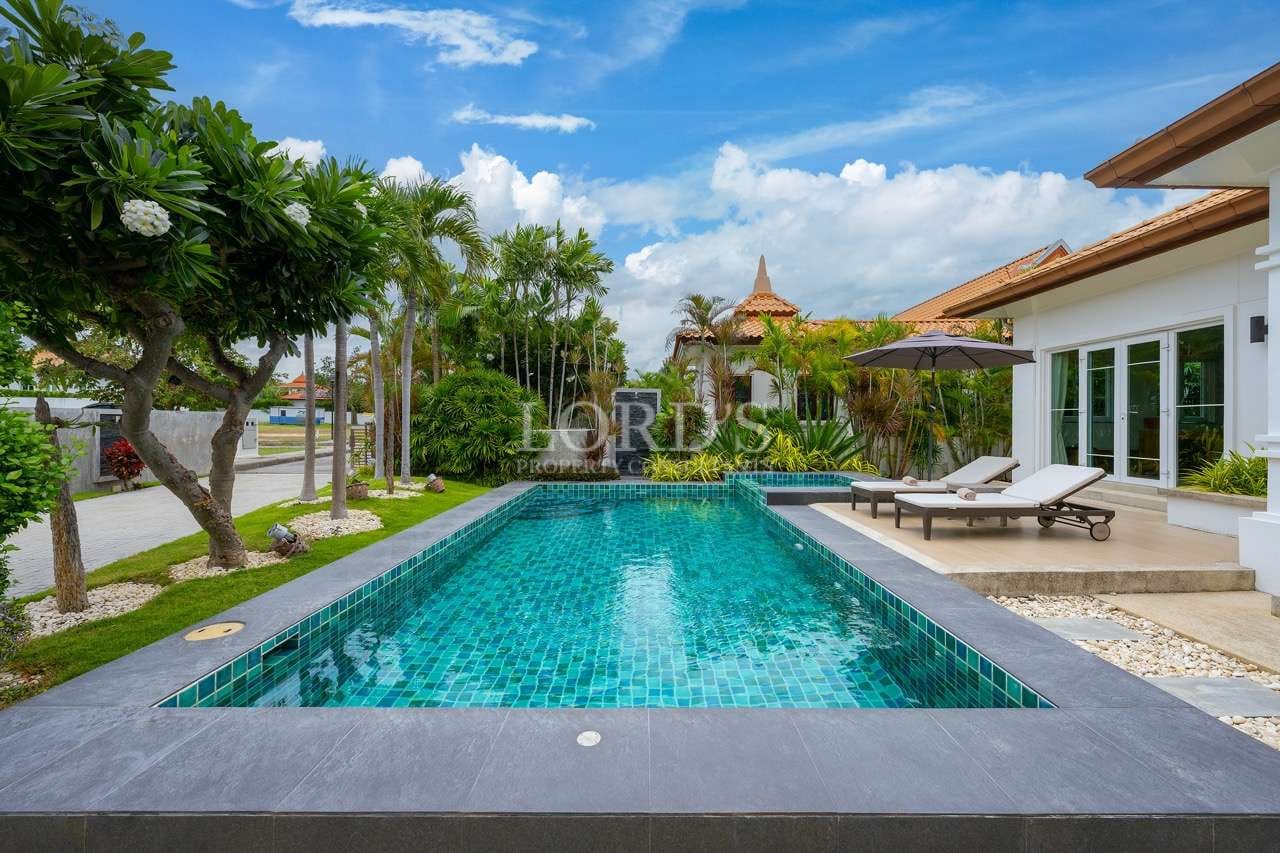 Luxury private swimming pool with tiled water, sun loungers, tropical garden, and modern villa exterior.