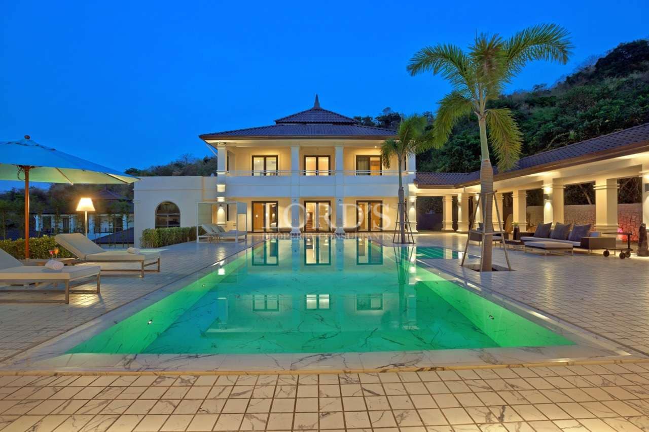 Luxury villa with illuminated swimming pool and outdoor lounge area at dusk.