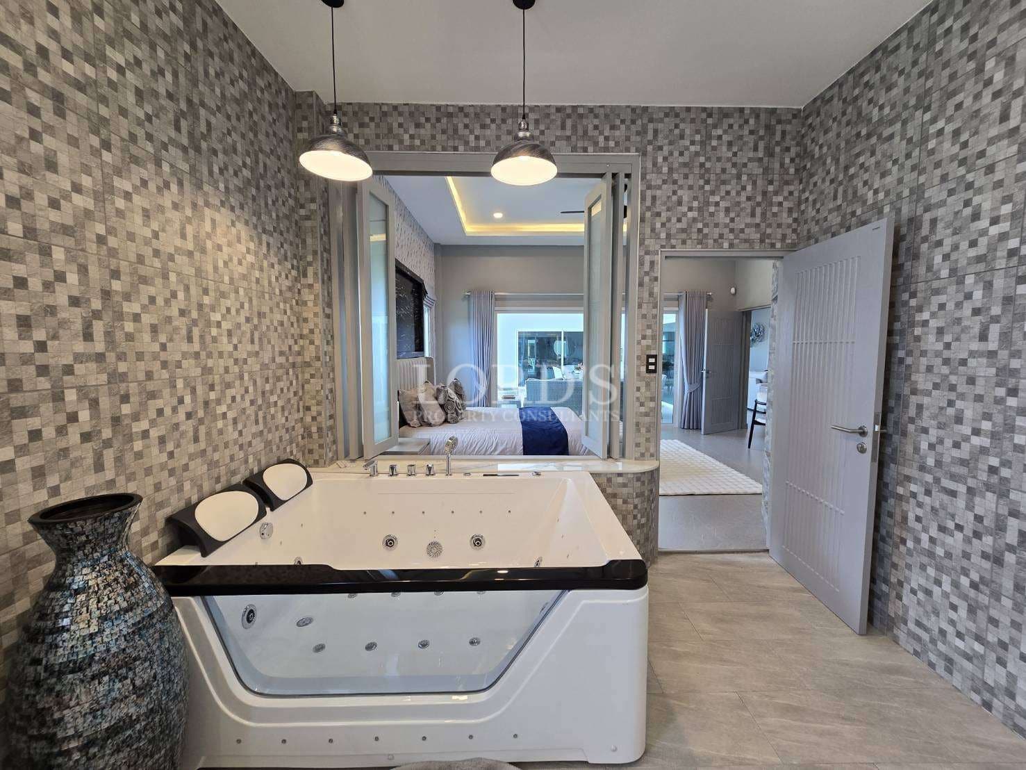 Luxury bathroom with jacuzzi bathtub, mosaic tile walls, pendant lighting, and bedroom view through open doors.