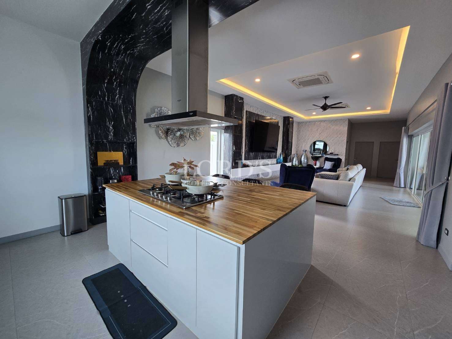 Luxury open-plan kitchen with central island, wooden countertop, built-in cooktop, and modern living area in the background.