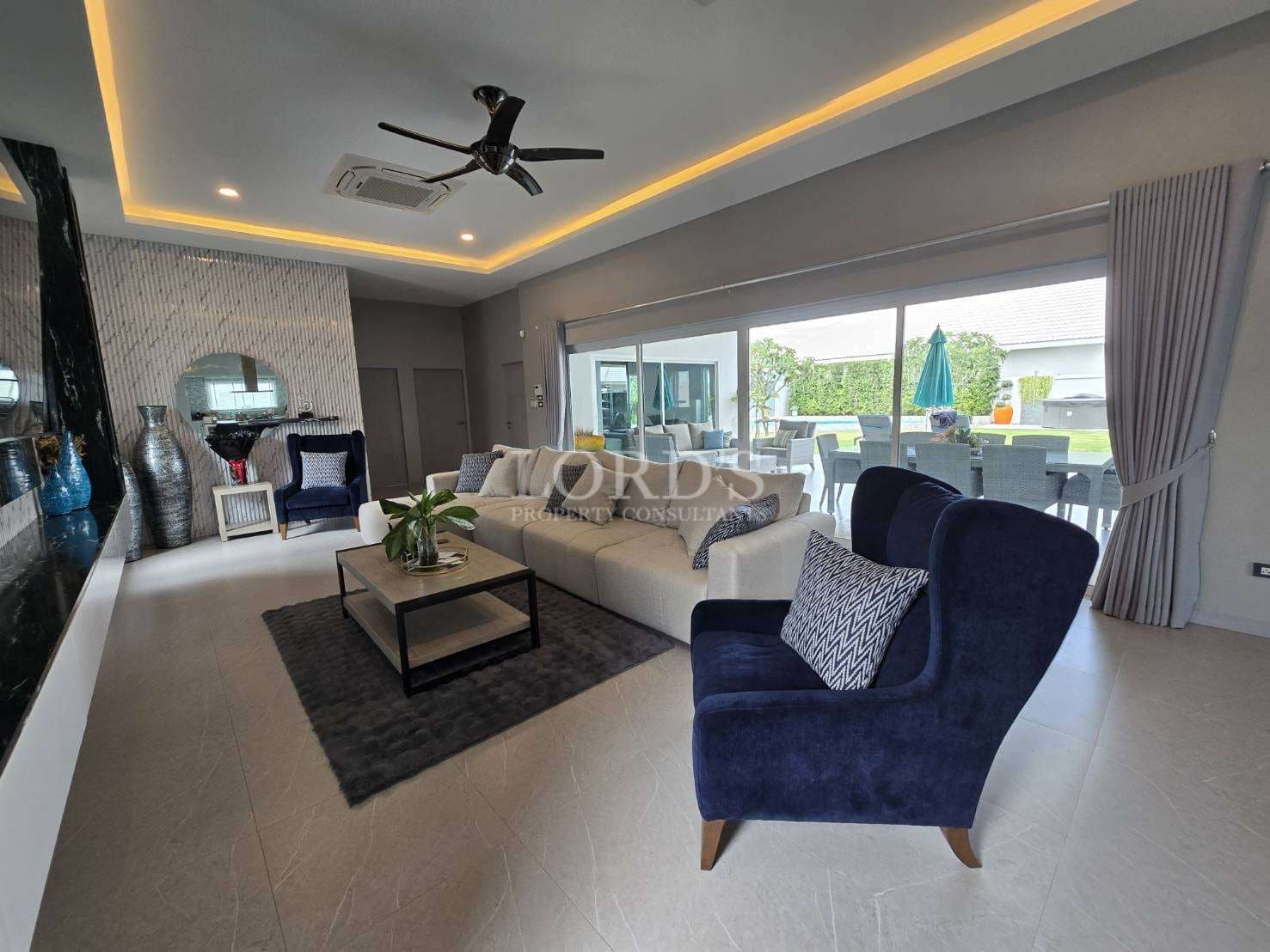 Luxury living room with open layout, plush seating, LED ceiling lighting, ceiling fan, and sliding glass doors to outdoor area.