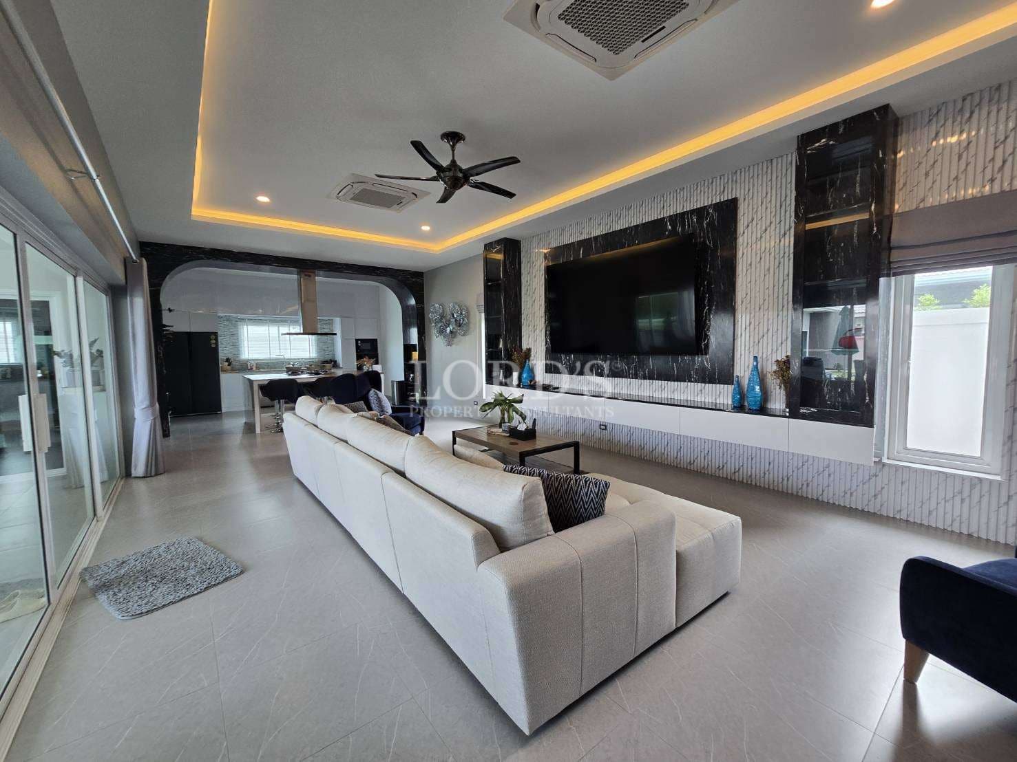 Luxury open-plan living room with sectional sofa, wall-mounted TV, LED ceiling lighting, and modern interior design.