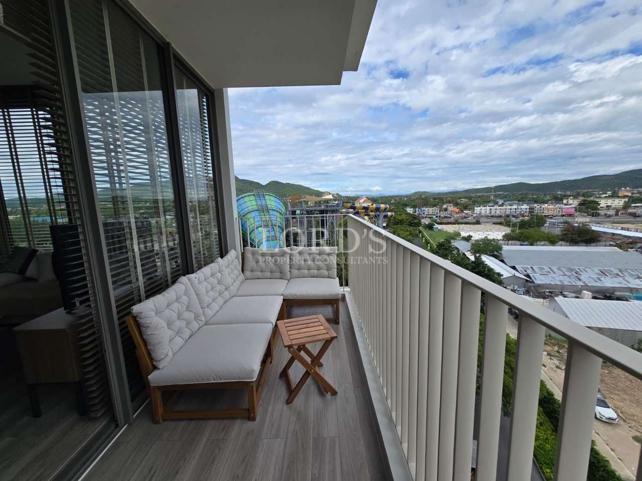 Private balcony with outdoor seating, city and hillside views, glass sliding doors, and modern apartment design.
