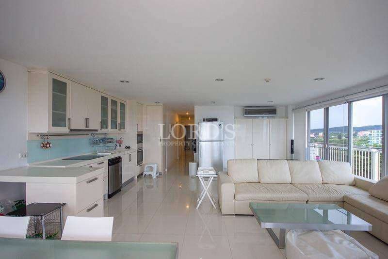Open-plan living area with modern kitchen, white sofa, glossy tiled floor, and large balcony windows