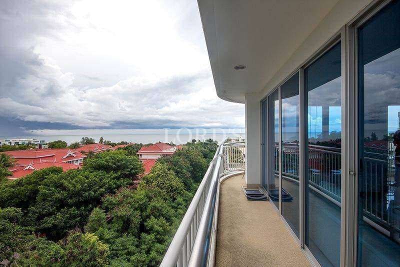 Curved balcony with glass doors overlooking treetops, rooftops, and ocean horizon