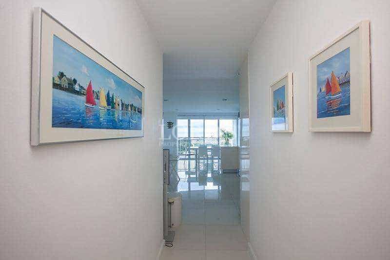 Bright hallway with framed wall art, glossy tiled floor, and natural light from living area