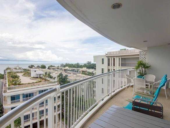 Curved balcony with outdoor seating overlooking ocean and modern residential buildings