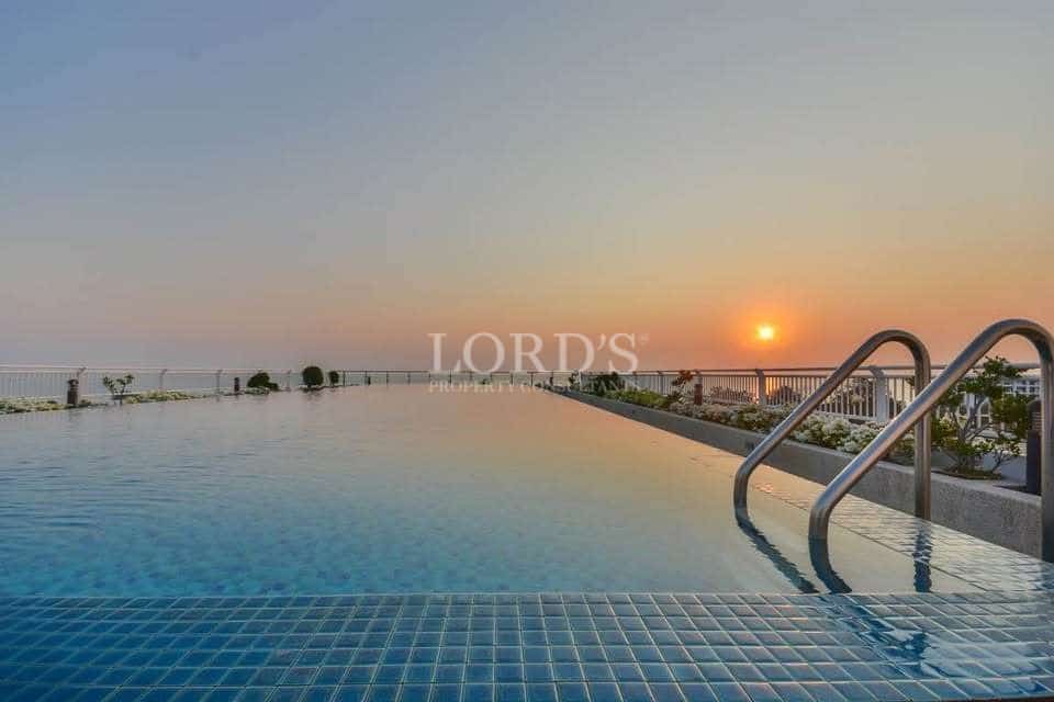 Rooftop infinity swimming pool at sunset with ocean view and stainless steel ladder