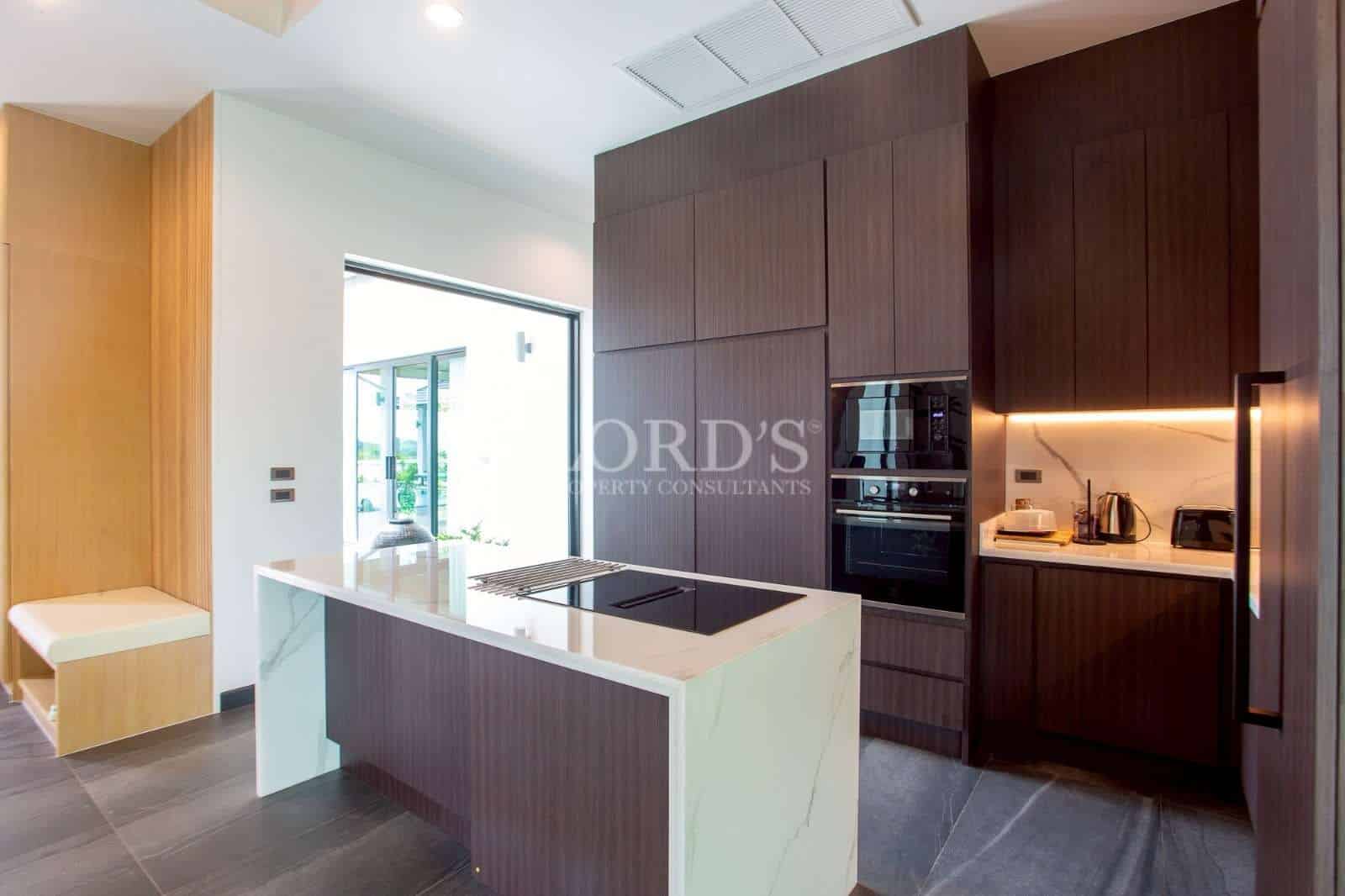 Modern kitchen with marble island, built-in appliances, and dark wood cabinetry.