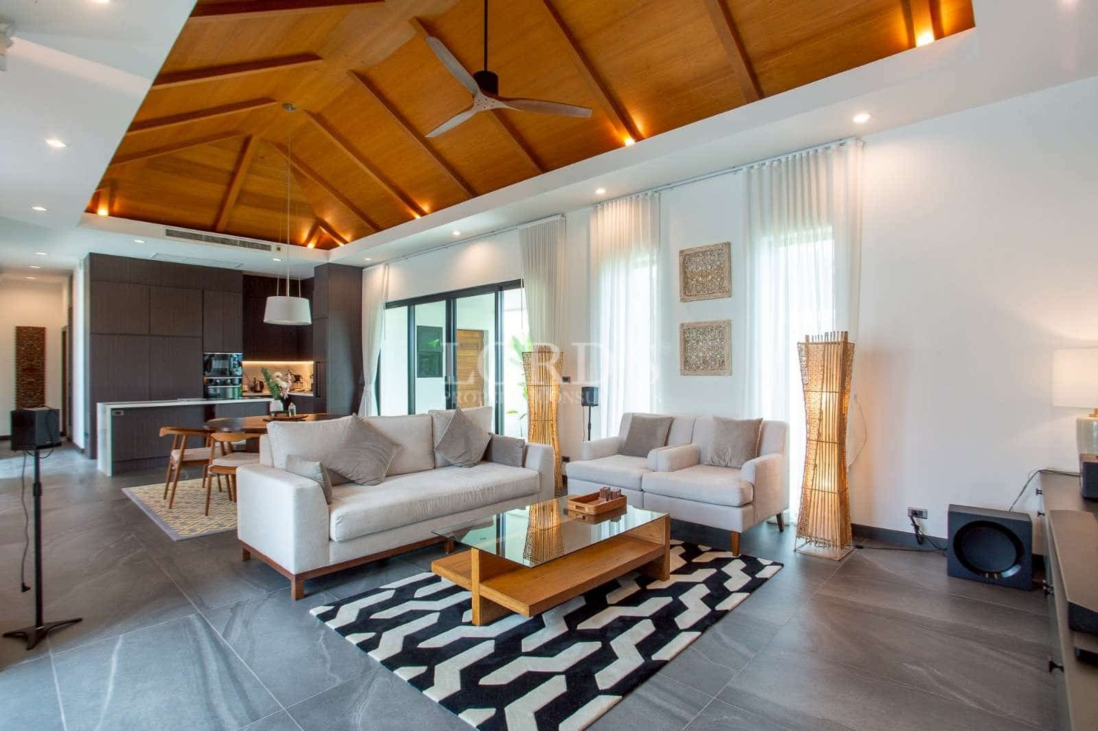 Modern open-plan living room with wooden ceiling, contemporary sofas, and integrated kitchen area.
