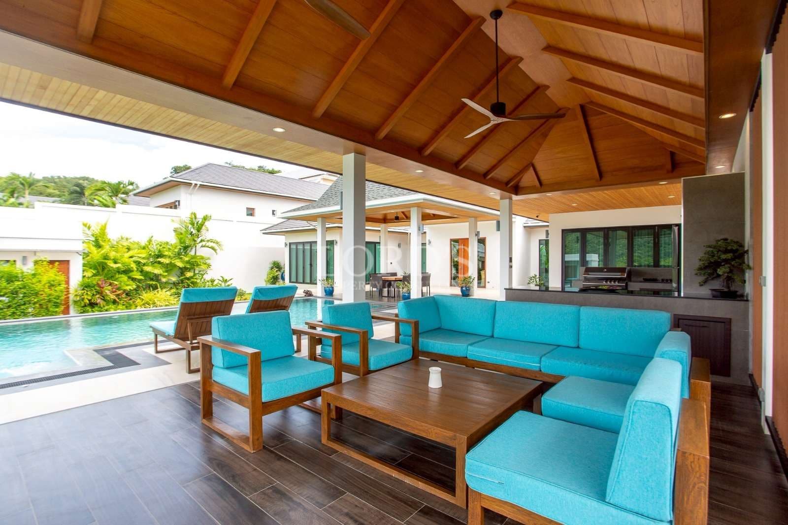 Luxury outdoor lounge with turquoise seating, wooden ceiling, and private pool in a modern villa.