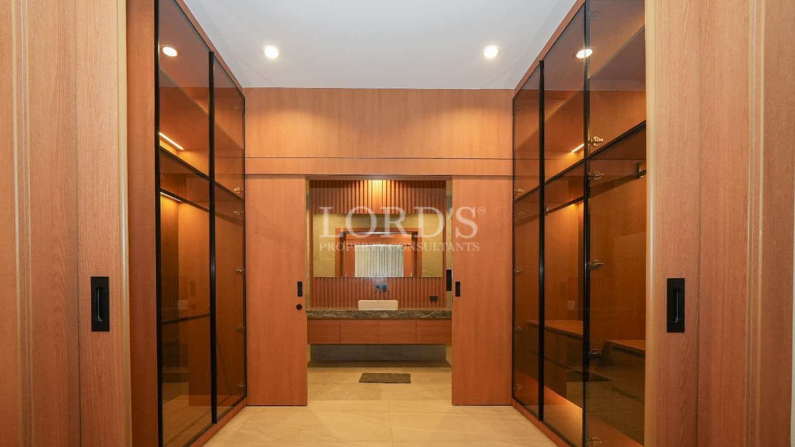 Luxury walk-in wardrobe with wooden cabinetry, glass-front storage, and warm recessed lighting.