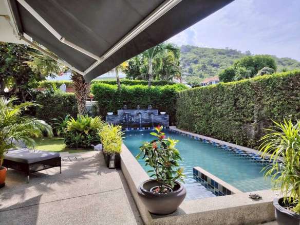 Private swimming pool with shaded patio, tropical plants, privacy hedges, and hillside views.