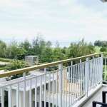 Private balcony with railing overlooking landscaped gardens, greenery, and open natural views.