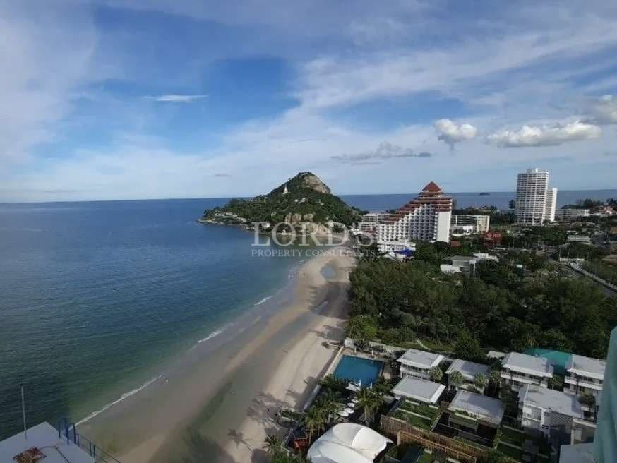 Panoramic ocean view overlooking sandy beach, hillside, and beachfront resorts under a blue sky.