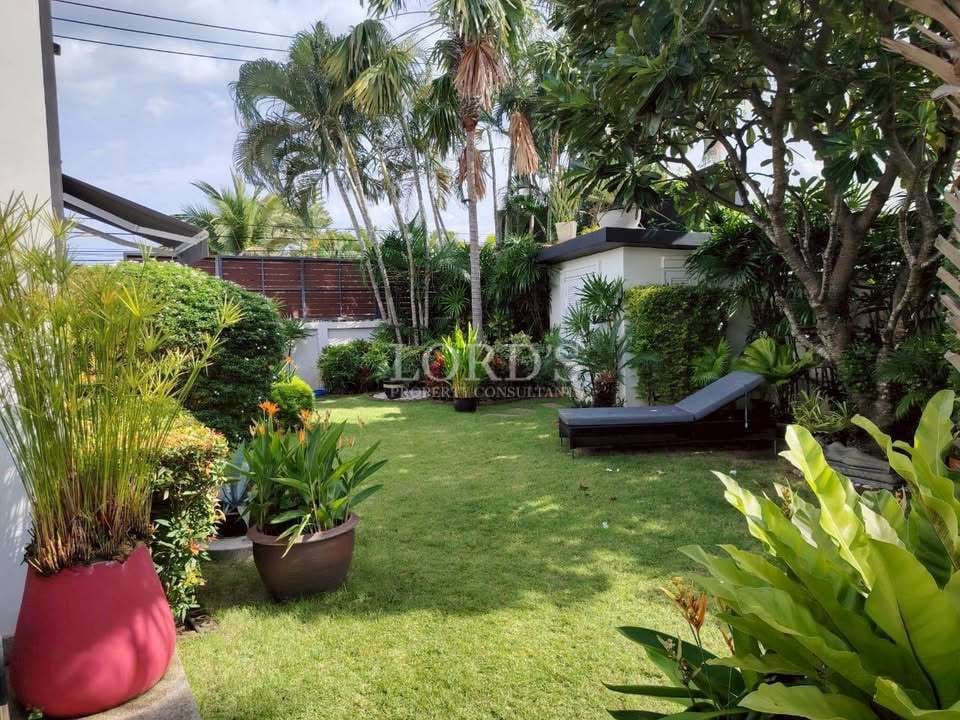 Private tropical garden with manicured lawn, palm trees, and outdoor sun lounger.