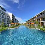 Luxury residential swimming pool between modern apartment buildings with landscaped gardens and clear blue water.