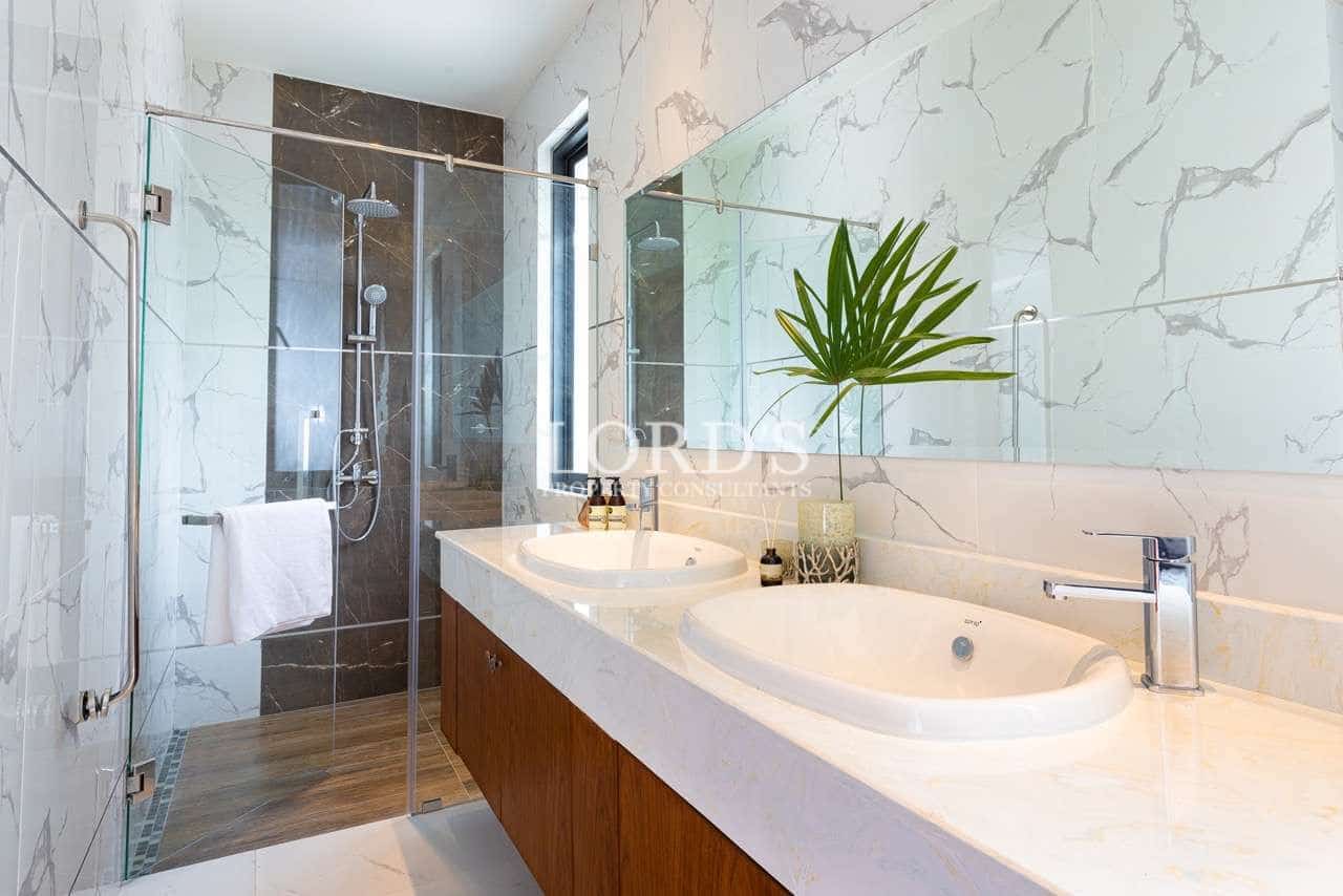 Modern bathroom with double sink vanity, glass shower enclosure, marble-style tiles, and chrome fixtures.