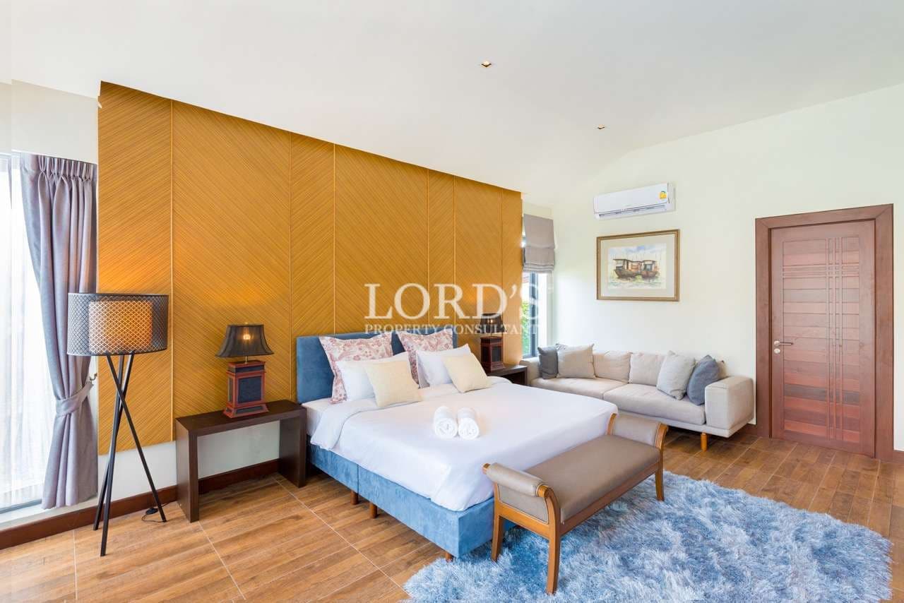 Luxury bedroom with king-size bed, wooden accent wall, seating area, and soft ambient lighting.