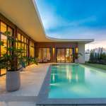 Modern luxury villa with private swimming pool, landscaped garden, and sunset lighting.