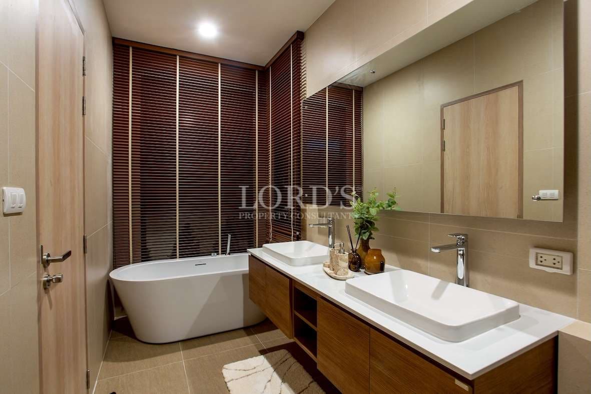 Modern bathroom with freestanding bathtub, double vanity, wooden cabinets, and warm ambient lighting.
