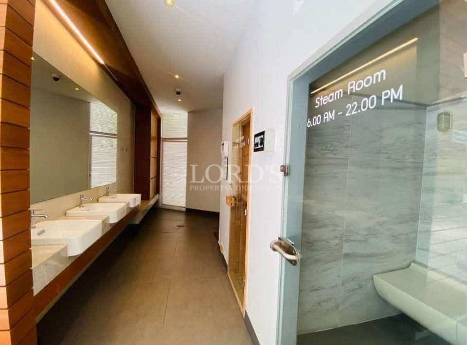 Modern steam room entrance with glass door, tiled interior, and shared washbasin area.