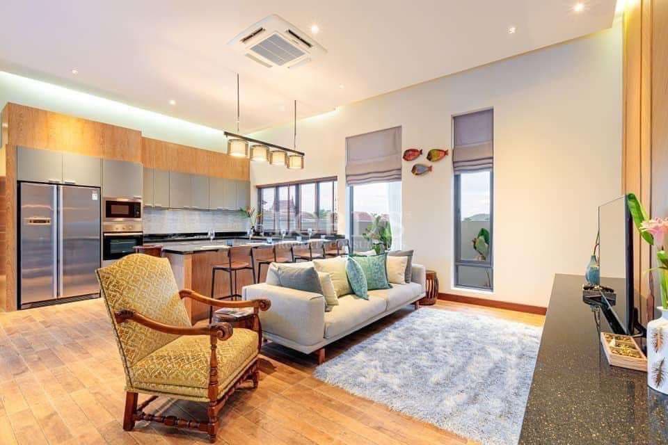 Modern open-plan living room and kitchen with island counter, wooden flooring, and contemporary furniture.