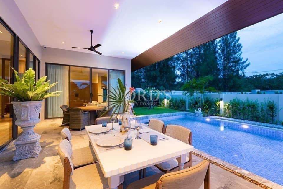 Luxury villa outdoor dining area with private swimming pool, covered terrace, and evening lighting.