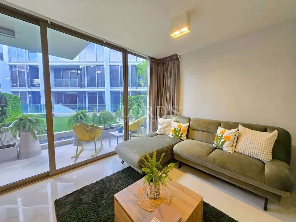 Modern living room with green sofa, sliding glass doors, and balcony overlooking landscaped garden.