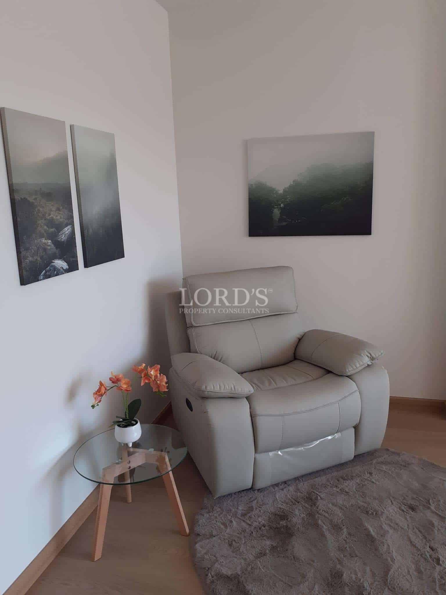 Modern reading corner with comfortable armchair, round glass side table, wall art, and soft rug