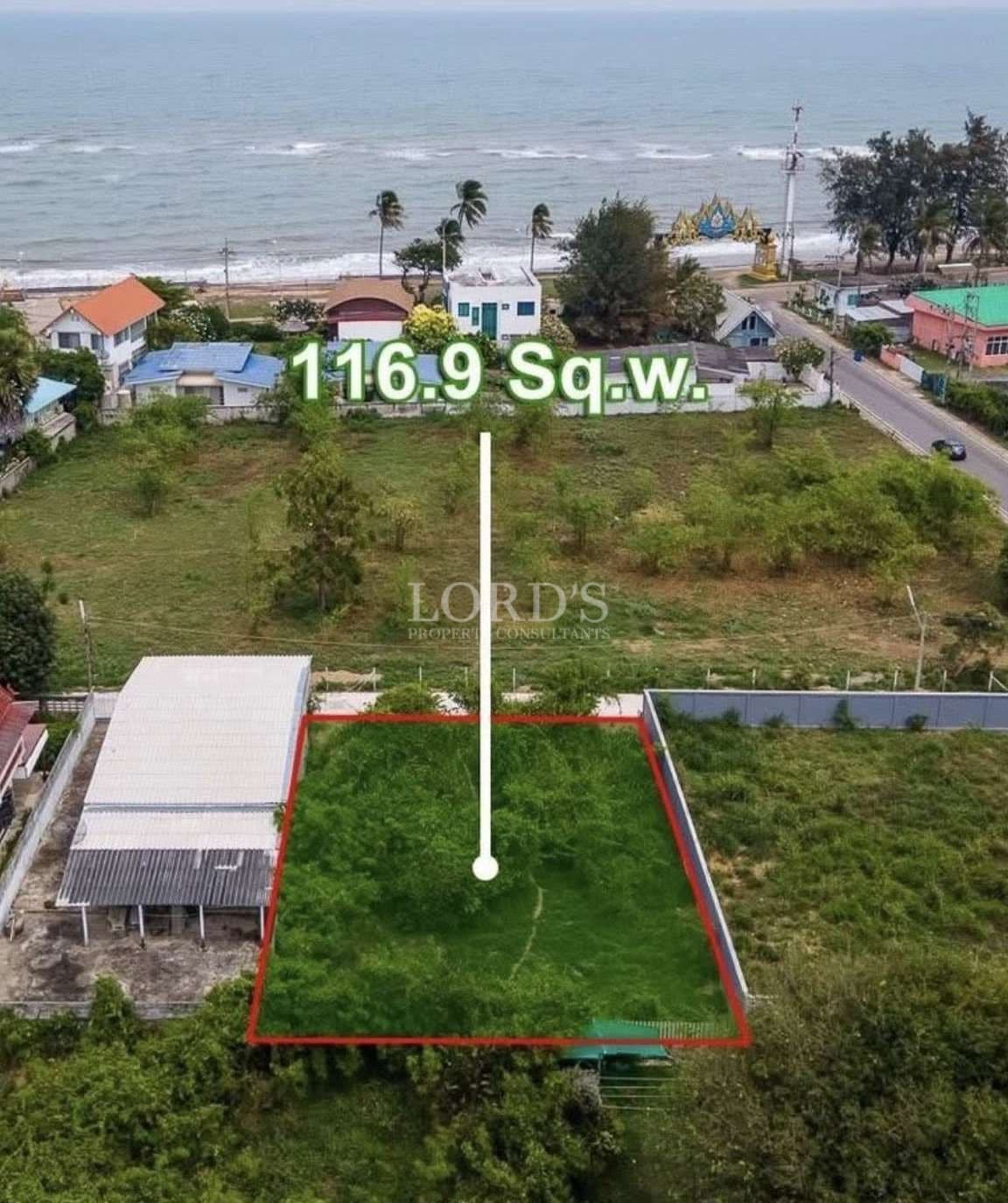 Aerial view of a 116.9 square wah land plot near the beach, outlined in red with surrounding houses and coastal road.