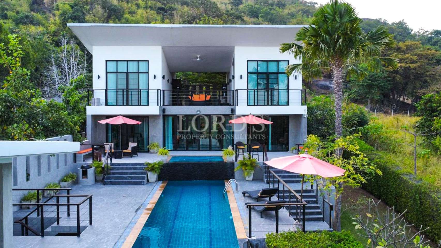 Modern two-story luxury villa with a private swimming pool and terraces surrounded by lush greenery.