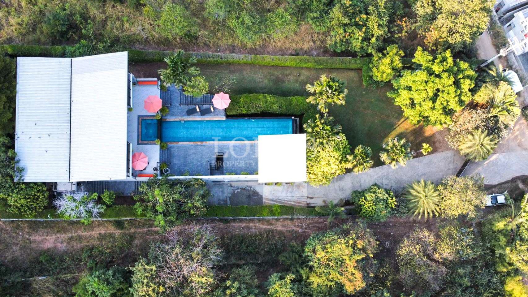 Aerial top-down view of a modern villa with a long swimming pool, garden, and surrounding greenery.