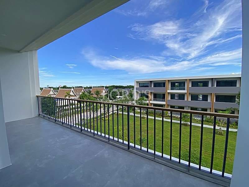 Spacious apartment balcony with tiled flooring overlooking landscaped green lawns and modern residential buildings.