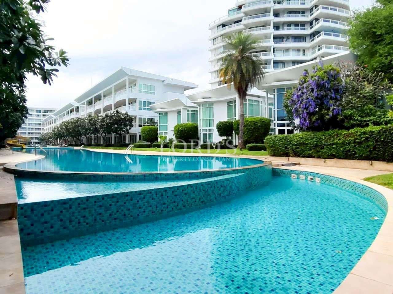 Luxury condominium swimming pool surrounded by modern white buildings and landscaped gardens.