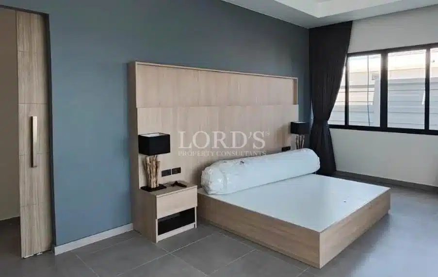 Modern minimalist bedroom with wooden bed frame, large headboard, bedside table, and natural light.