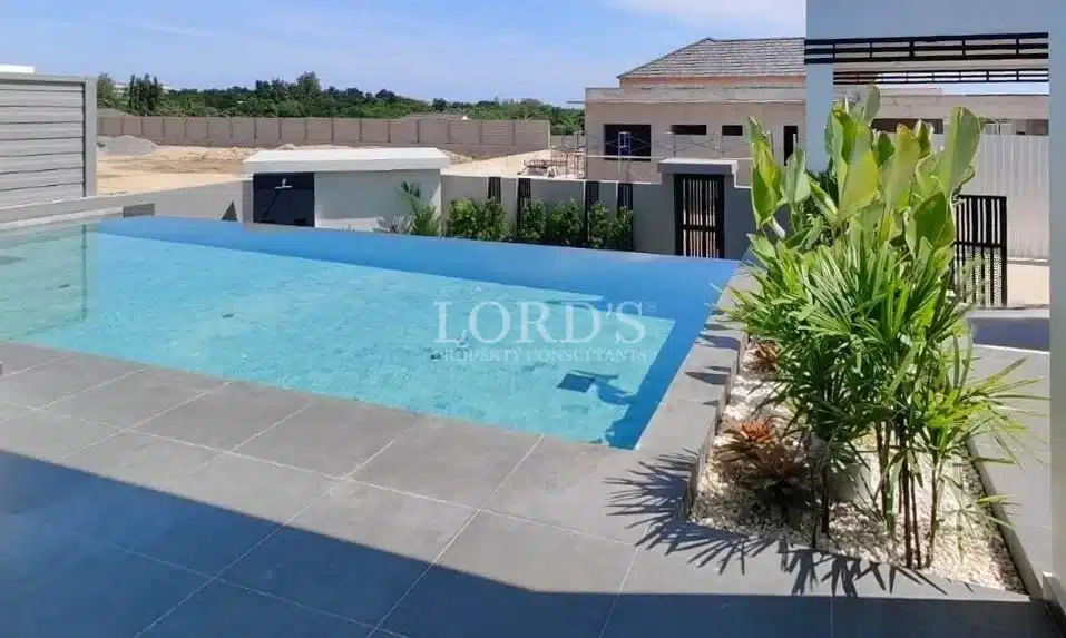 Modern outdoor swimming pool with tiled deck, landscaped plants, and contemporary residential setting.