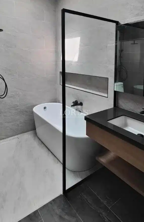 Modern bathroom with freestanding bathtub, glass partition, black fixtures, and stone tile walls.