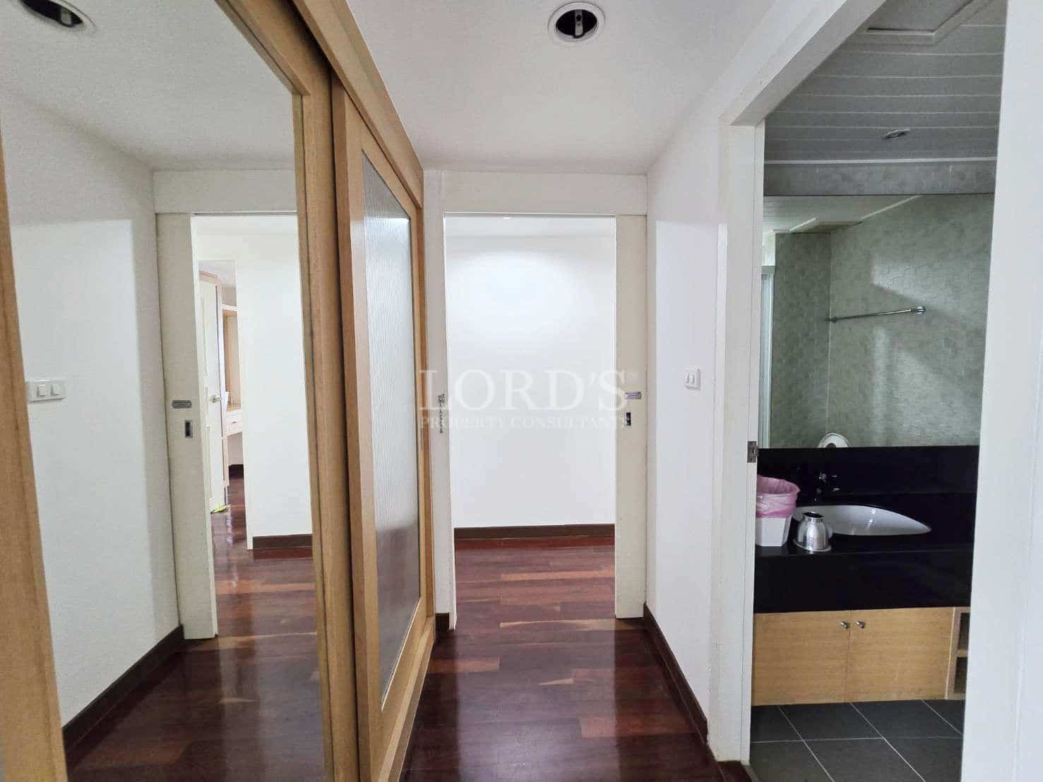 Bright interior hallway with wooden floors, sliding door, and adjacent bathroom entrance.
