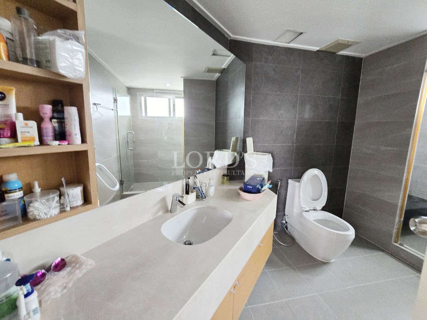 Modern bathroom with long vanity countertop, built-in storage shelves, and glass-enclosed shower.