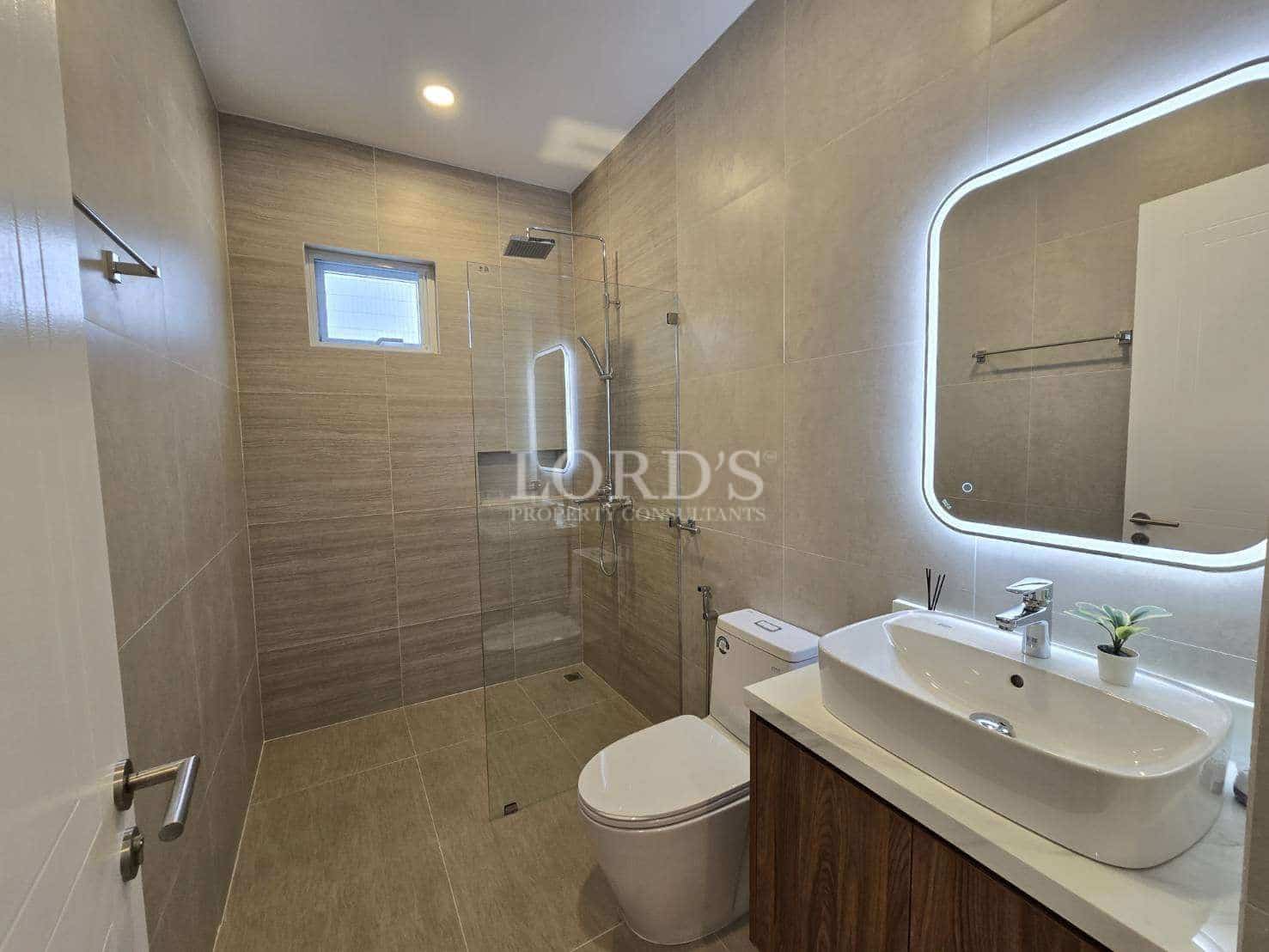 Modern bathroom with walk-in glass shower, rainfall showerhead, vanity sink, illuminated mirror, and neutral tile finishes.