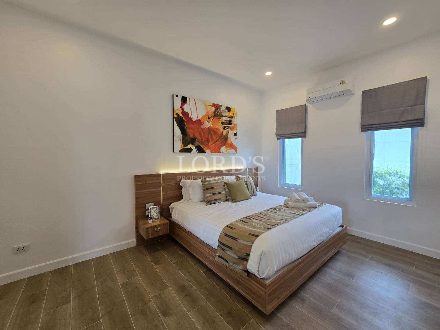 Modern bedroom with a double bed, wooden flooring, abstract wall art, air conditioning, and natural light.