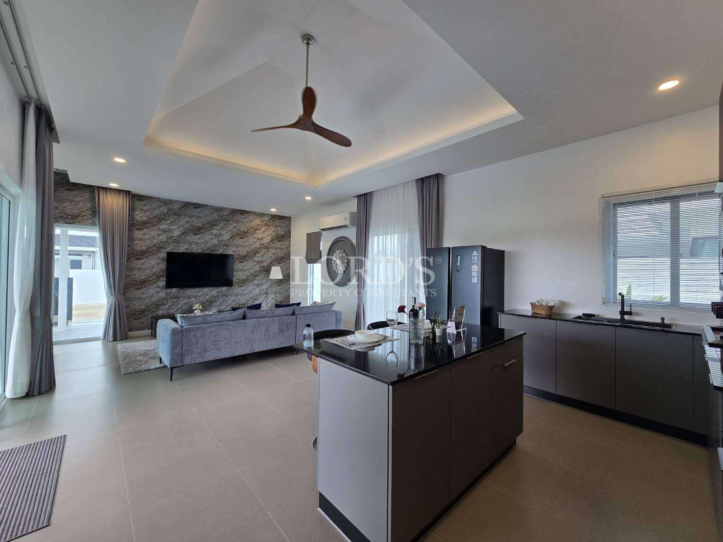 Modern open-plan living room and kitchen with island, marble accent wall, and ceiling fan.