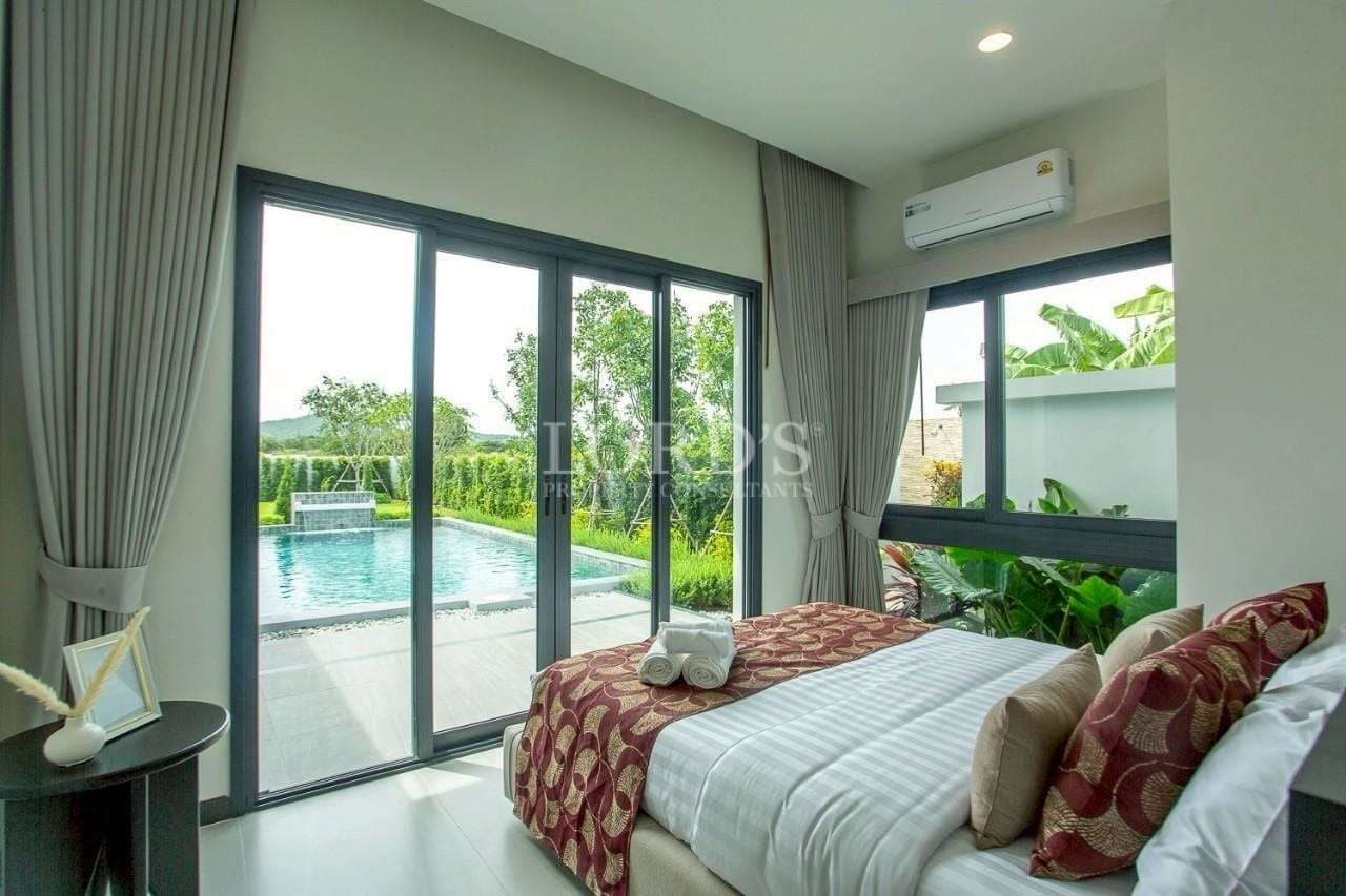 Modern bedroom with sliding glass doors overlooking a private swimming pool and garden.