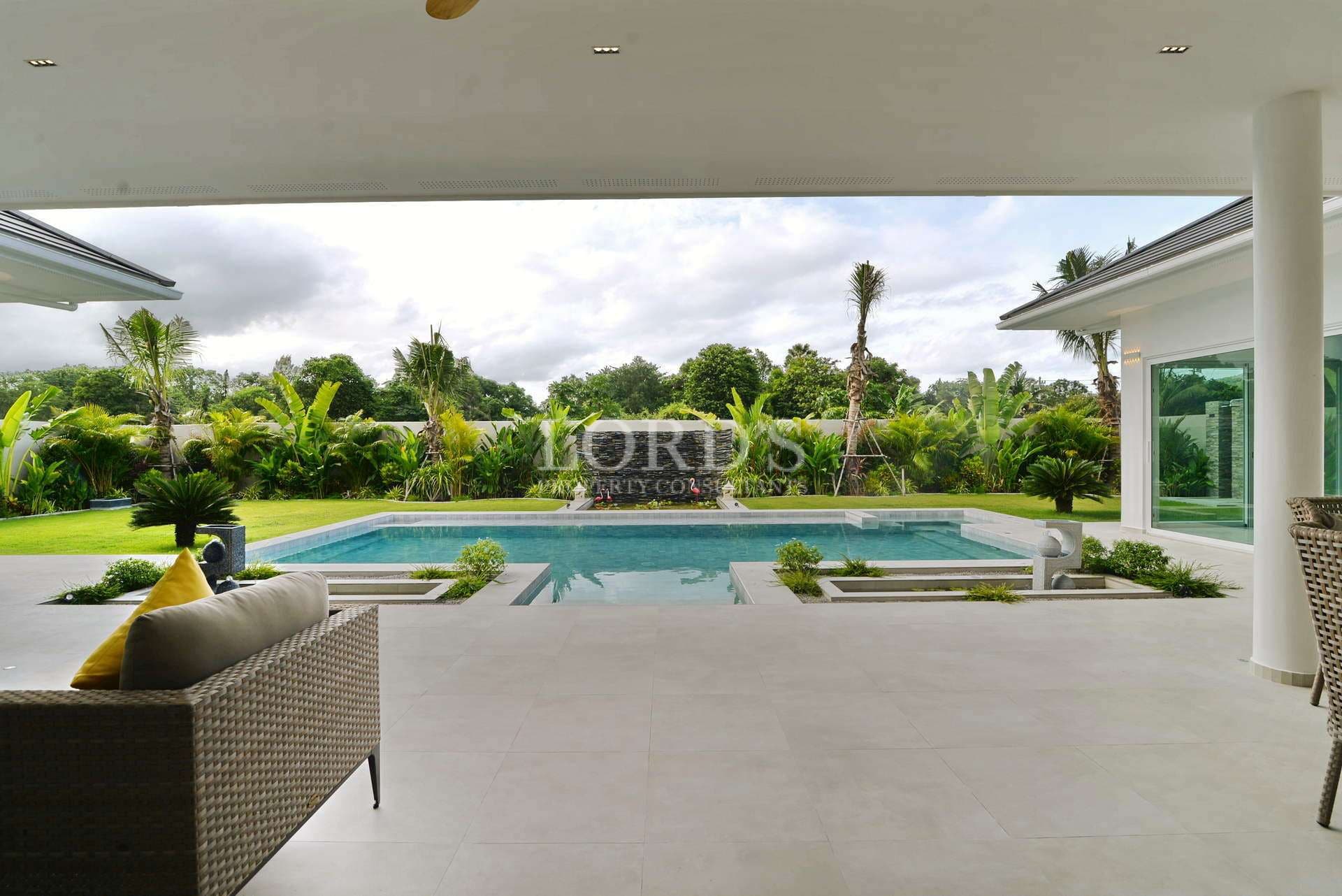 Covered outdoor lounge area overlooking a private swimming pool and lush tropical garden.