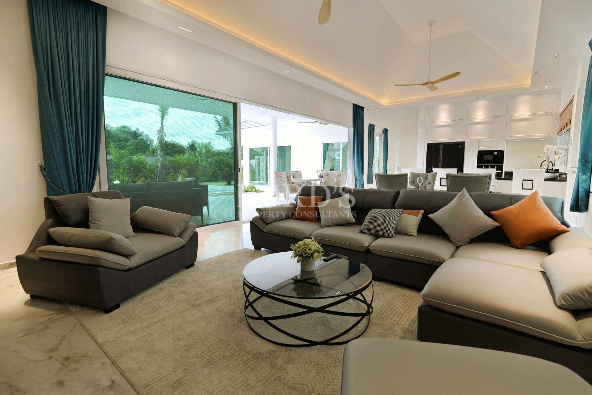 Modern open-plan living room with sectional sofa, glass doors, marble floors, and garden views.