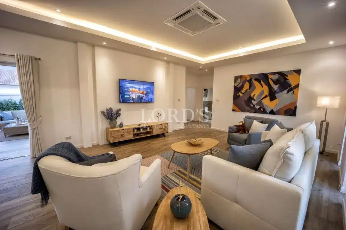 Contemporary living room with wall-mounted TV, neutral sofas, wooden coffee table, and recessed LED ceiling lighting.