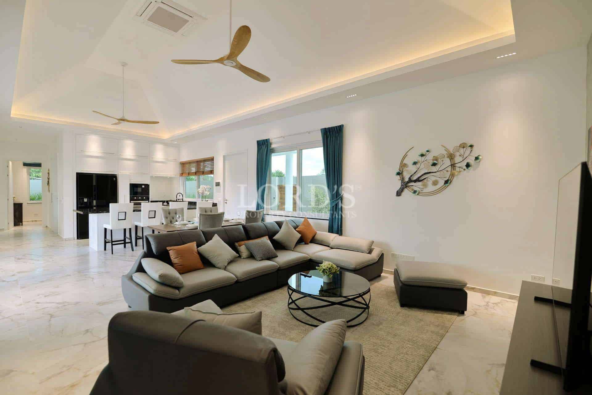 Spacious modern living room with sectional sofa, marble flooring, ceiling fans, and open-plan kitchen.