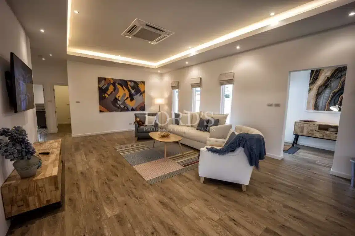 Modern living room with neutral sofas, wooden flooring, recessed LED ceiling lights, and abstract wall art.