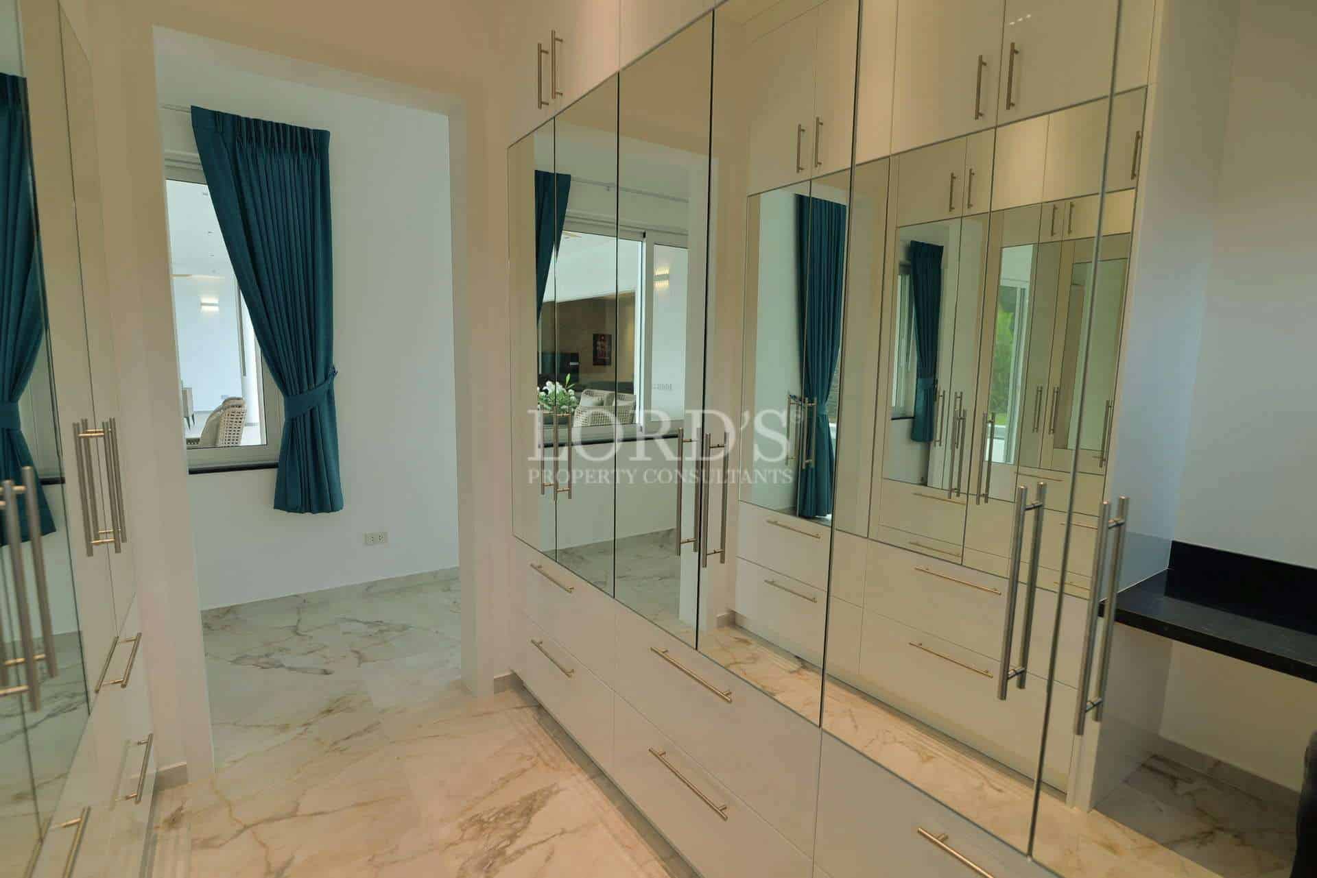Modern walk-in wardrobe with mirrored cabinets, built-in drawers, and marble flooring.